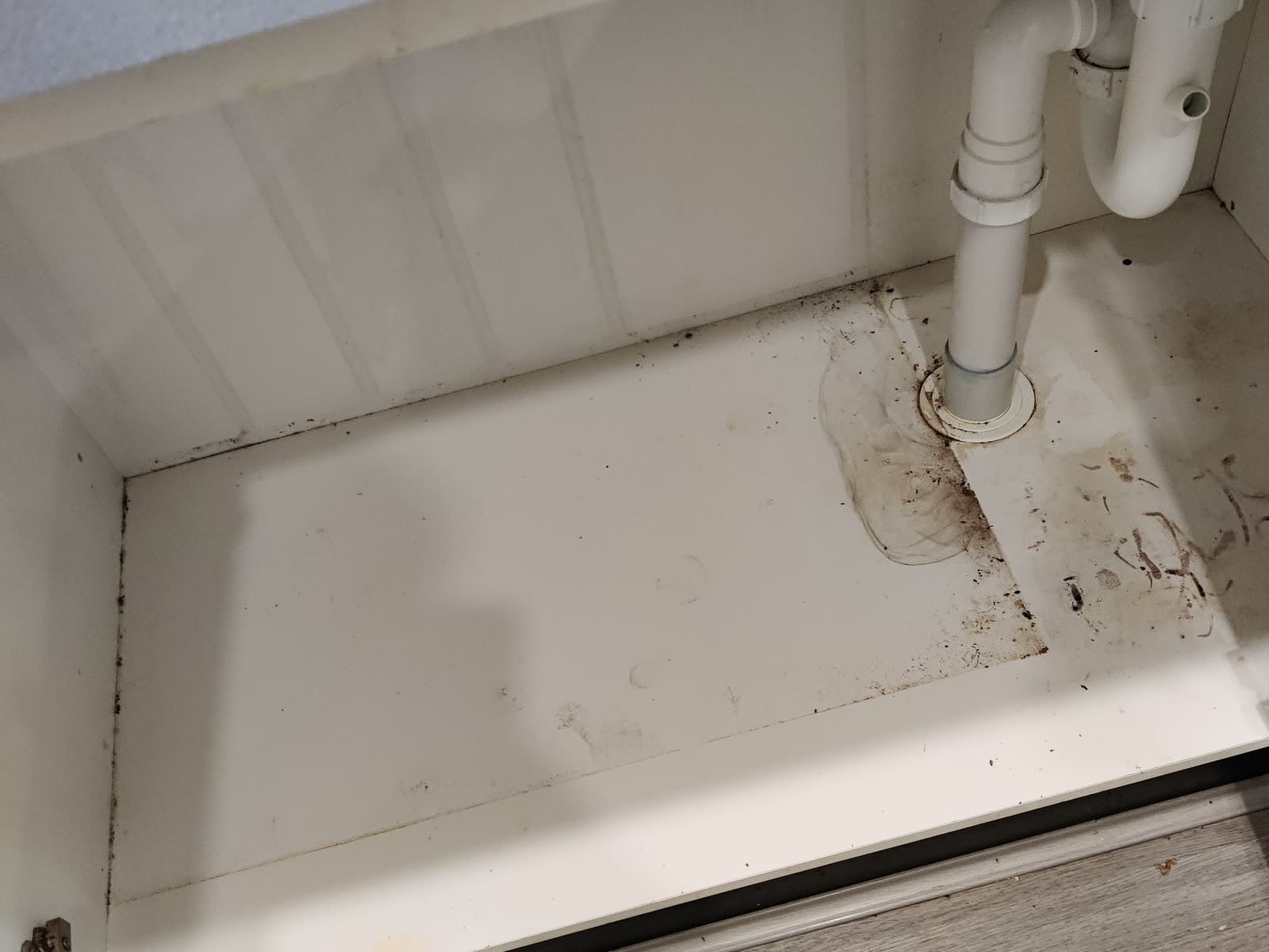 Stained, grimy cabinet base under a kitchen sink before cleaning